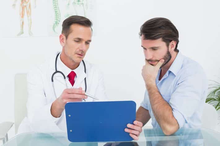 Male doctor discussing reports with patient at desk in medical o